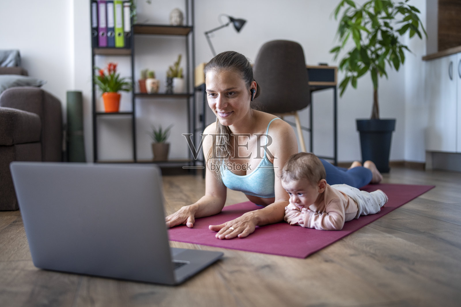 年轻妈妈一边用笔记本电脑一边和宝宝一起锻炼。照片摄影图片