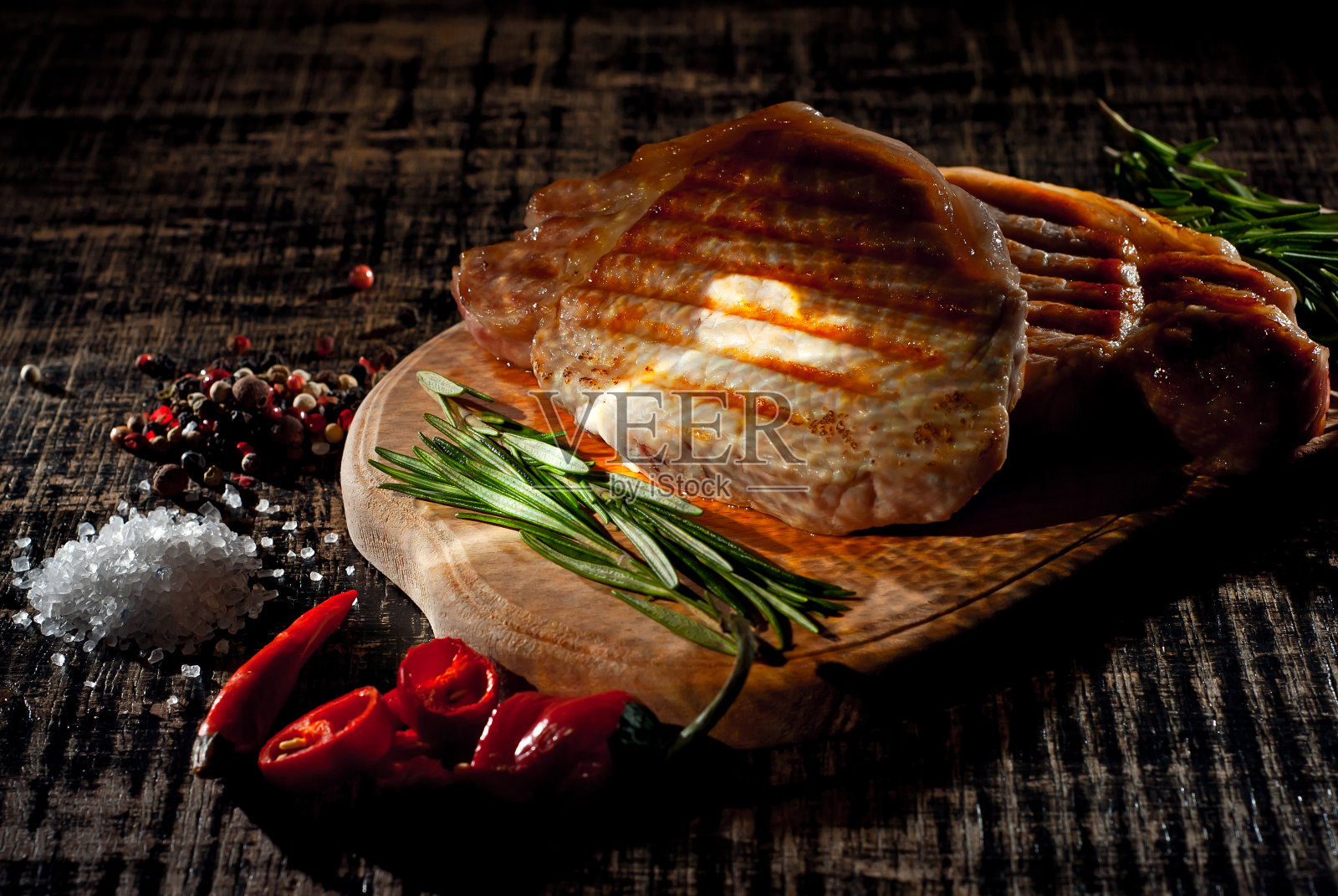 黑底木板上的牛排。一张破旧的桌子上放着烤肉。新鲜的迷迭香胡椒和盐放在牛排旁边。作为一种艺术效果来对比戏剧性的光线。照片摄影图片