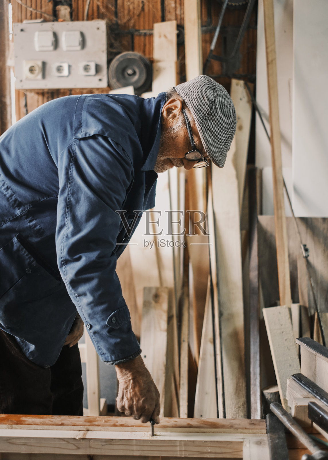 一个老木匠，他在一个旧车间里给木头钉螺丝钉。照片摄影图片
