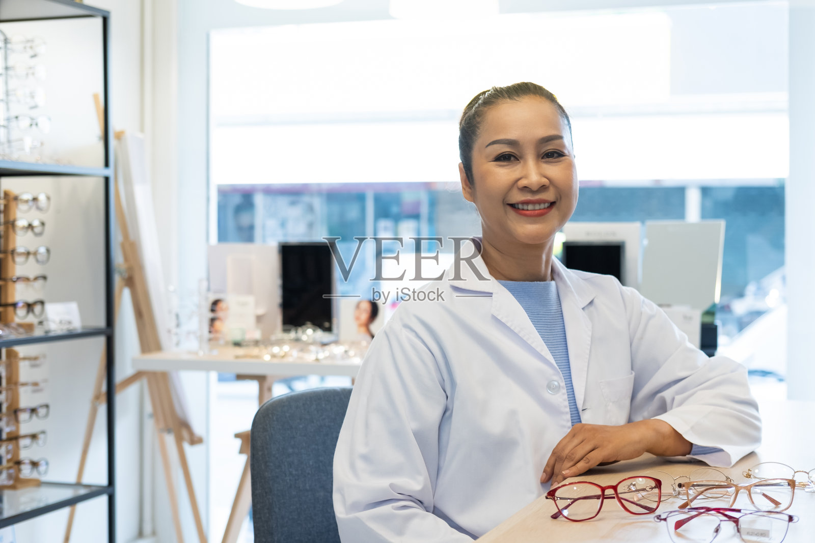 亚洲女性验光师微笑着使用平板电脑，并在眼镜店、专卖店内试用推荐客户选择眼镜美框。以病人为视，医疗理念。照片摄影图片