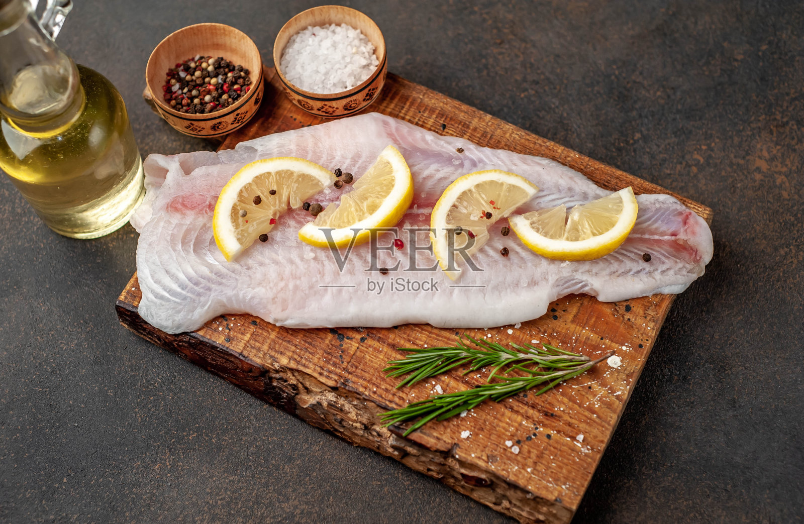 在切菜板上放上生pangasius鱼片，配以柠檬、油和香料，以石头为背景。生鱼。照片摄影图片