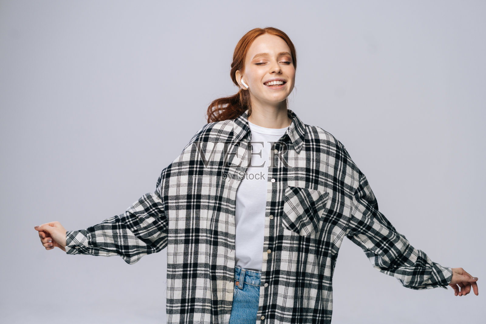 快乐的年轻女子戴着无线耳机边听流行歌曲边跳舞，闭着眼睛。照片摄影图片