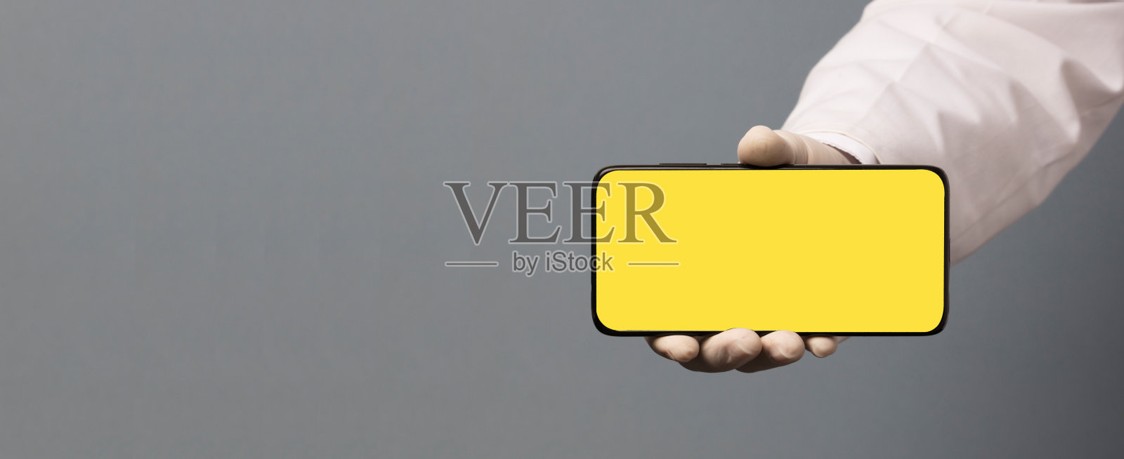 黑色手机在医生手中与黄色屏幕为模型，灰色背景照片摄影图片