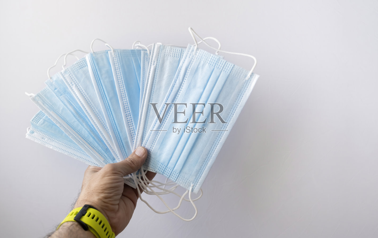 一只戴着黄色表带的手在白色背景上举着一组外科口罩照片摄影图片