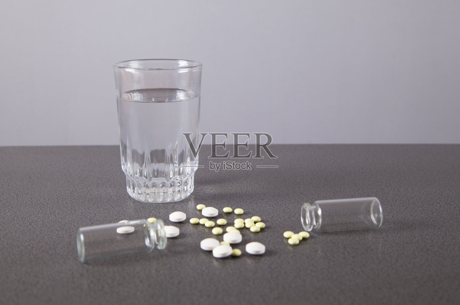 药片，瓶子和一杯水在灰色背景上。照片摄影图片