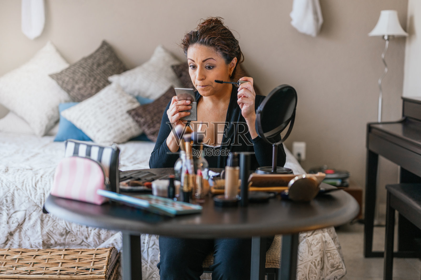 美女坐在化妆台上，她面前有一张桌子，上面放着许多化妆工具。照片摄影图片