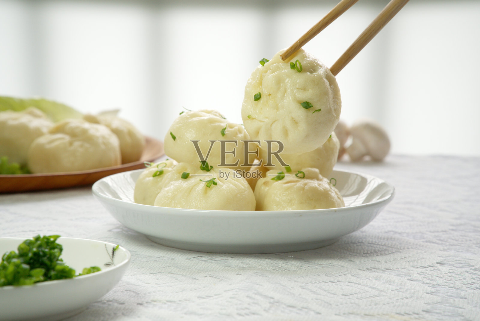 用筷子夹起一个白色盘子里的小圆面包，是中国传统的小麦食品照片摄影图片