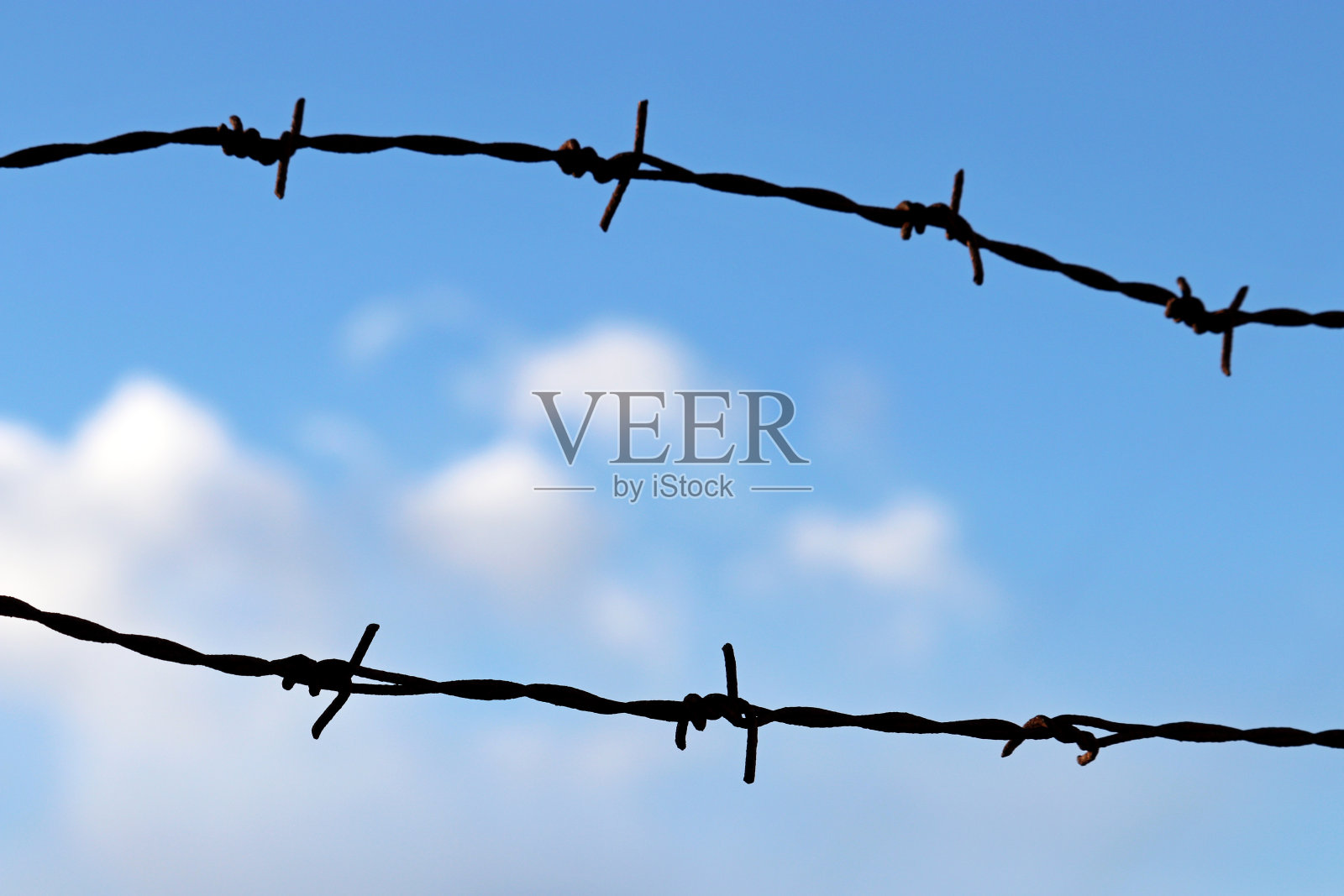 在蓝天白云的映衬下，生锈的铁丝网的剪影照片摄影图片