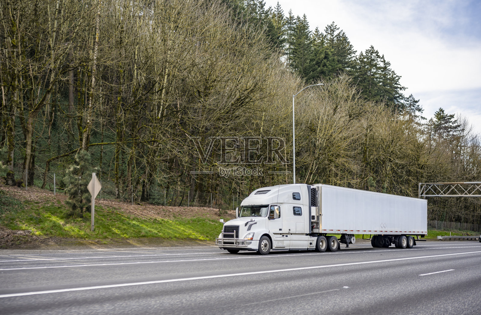 白色大卡车长途工业半挂车运输货物的冰箱半挂车运行在风景优美的公路与森林在山上照片摄影图片