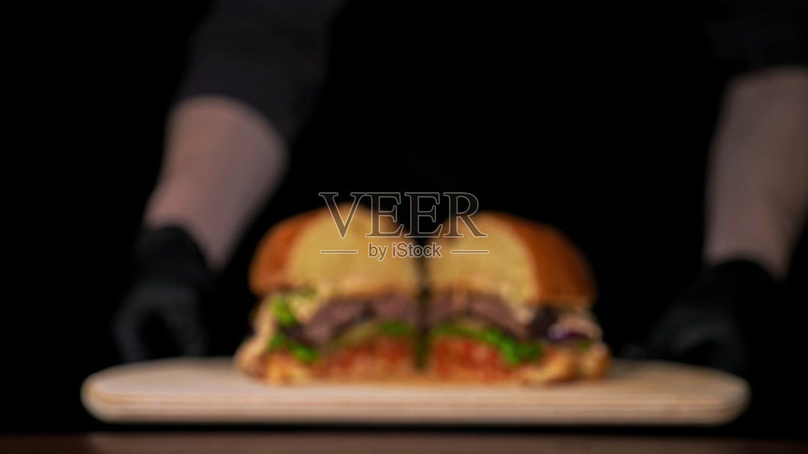 模糊的背景。切手工汉堡正在烹饪。由沙司，生菜，红洋葱，泡菜，奶酪，辣椒青椒，面包，大理石肉牛肉。照片摄影图片