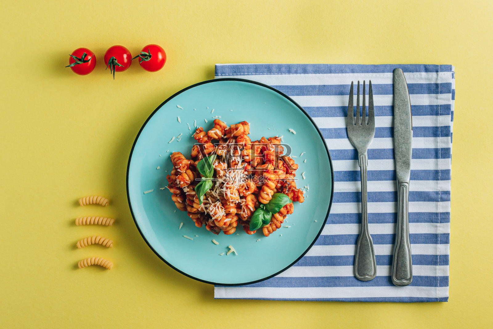 用一盘意大利面、番茄、罗勒、餐巾和餐具在黄色背景上组合而成。创意平面躺照片摄影图片