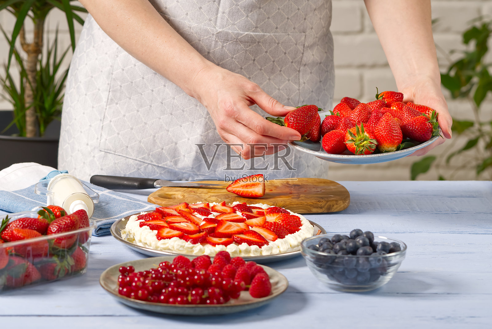女面包师把草莓堆在草莓蛋糕上。自制草莓蛋糕，由蛋白蛋糕和草莓奶油制成。照片摄影图片