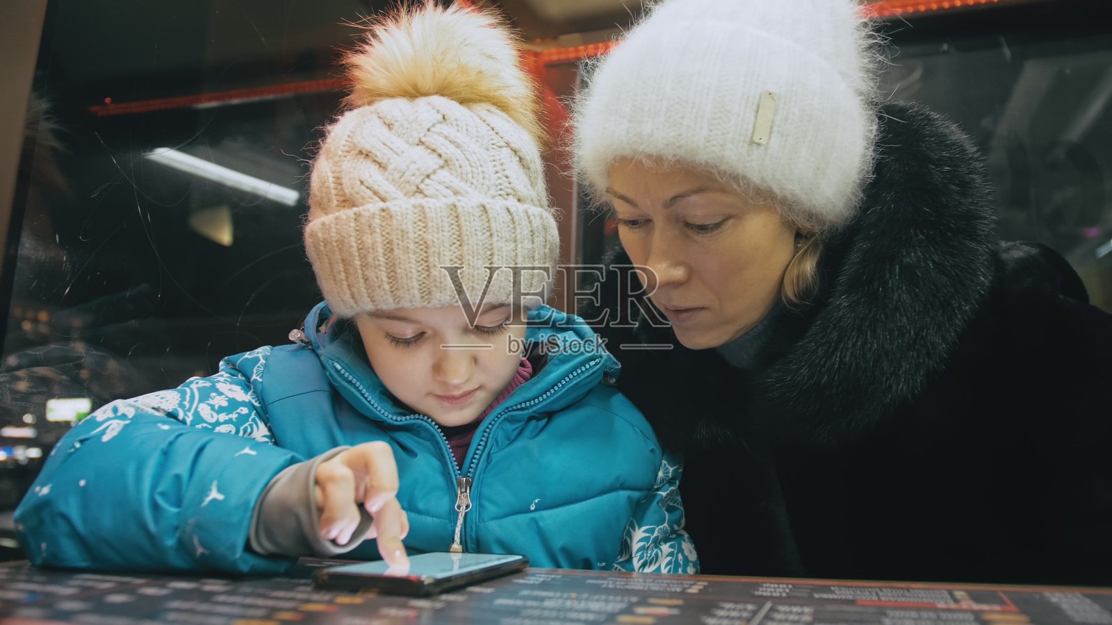 漂亮的白人母亲和女儿坐在咖啡馆里用智能手机。年长的儿童向妈妈展示和解释智能手机上的东西。照片摄影图片