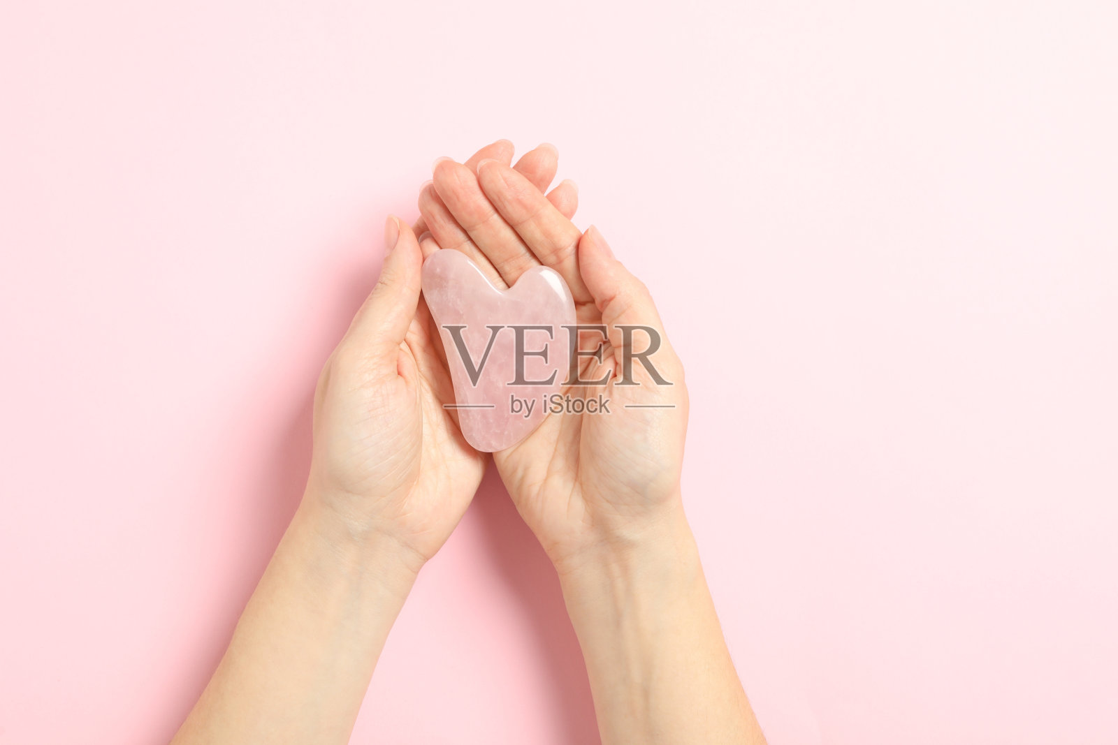 女子与玫瑰石英瓜沙工具在浅粉色的背景，特写照片摄影图片