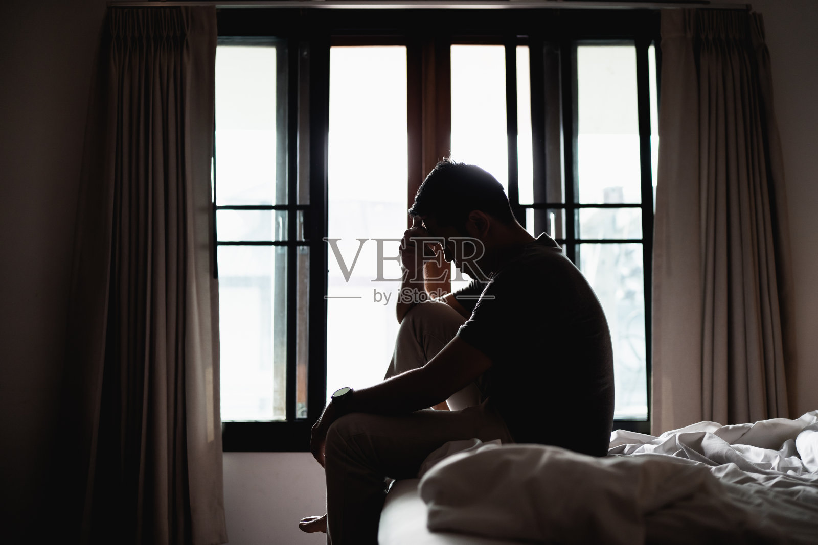 剪影抑郁的男人悲伤地坐在卧室的床上，抑郁的概念照片摄影图片