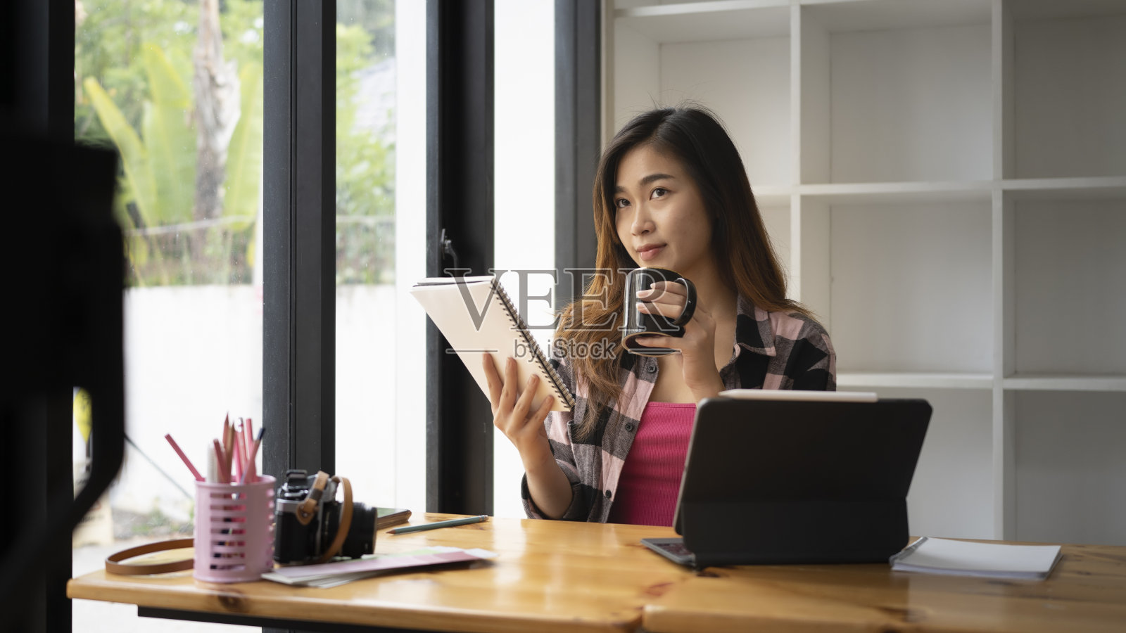 年轻的女设计师早上在办公室喝咖啡，用平板电脑看新闻。照片摄影图片