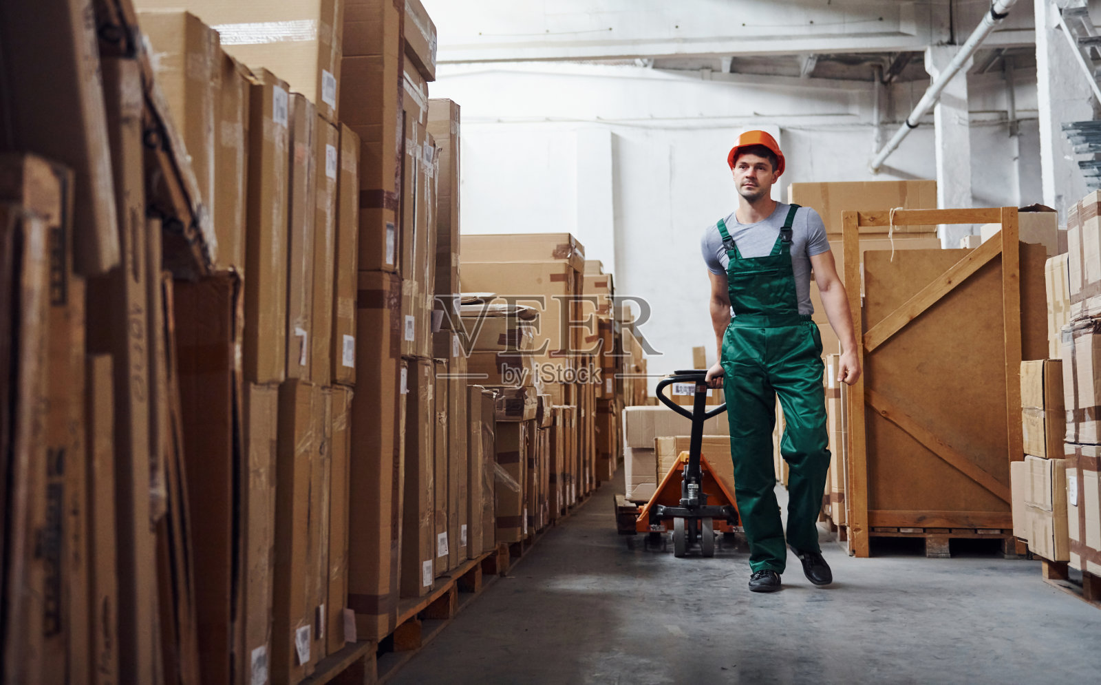 身着制服的年轻男性工人在仓库里用托盘卡车搬运货物照片摄影图片