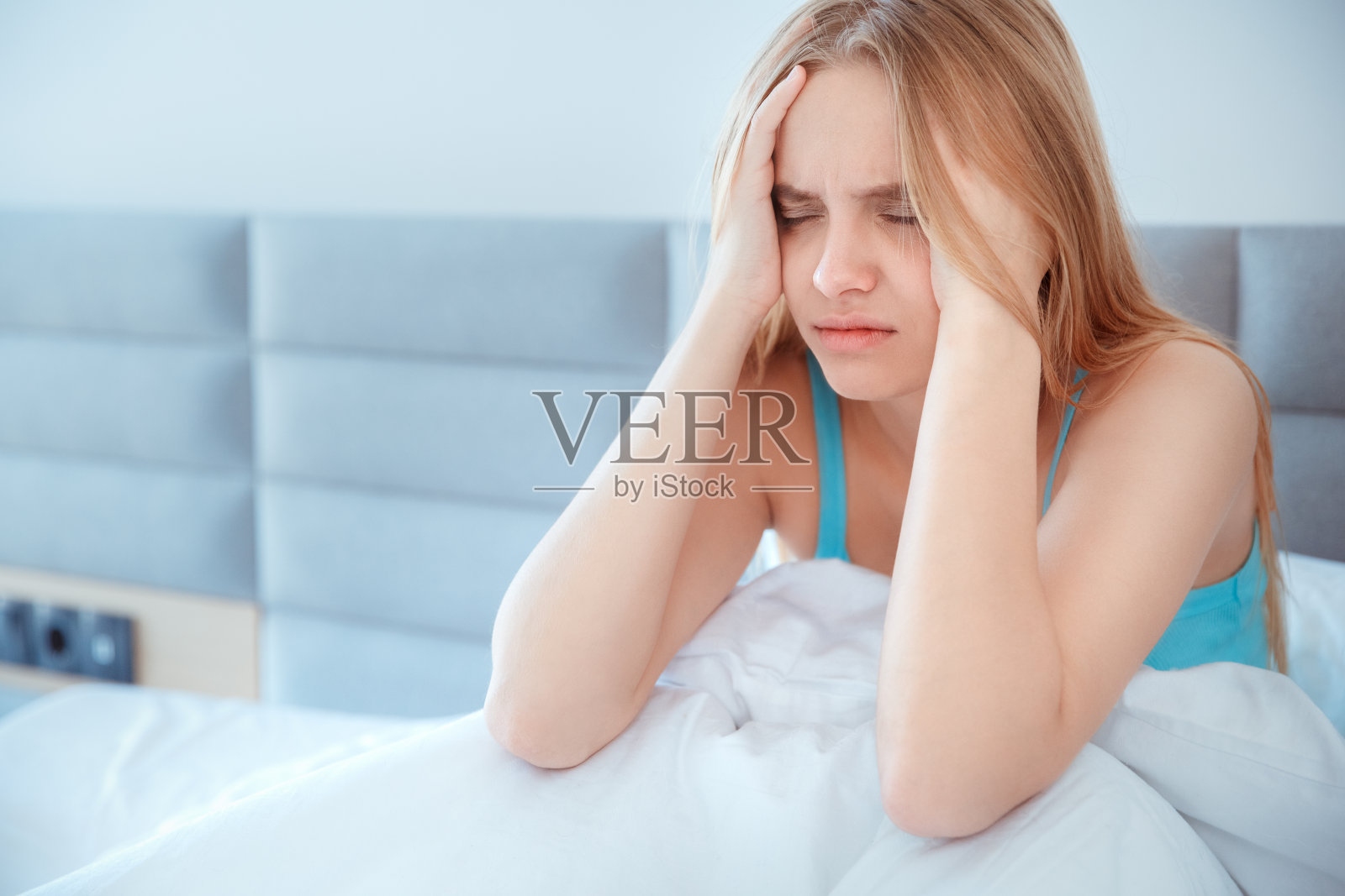 年轻女子坐在家里的床上，头痛醒了照片摄影图片