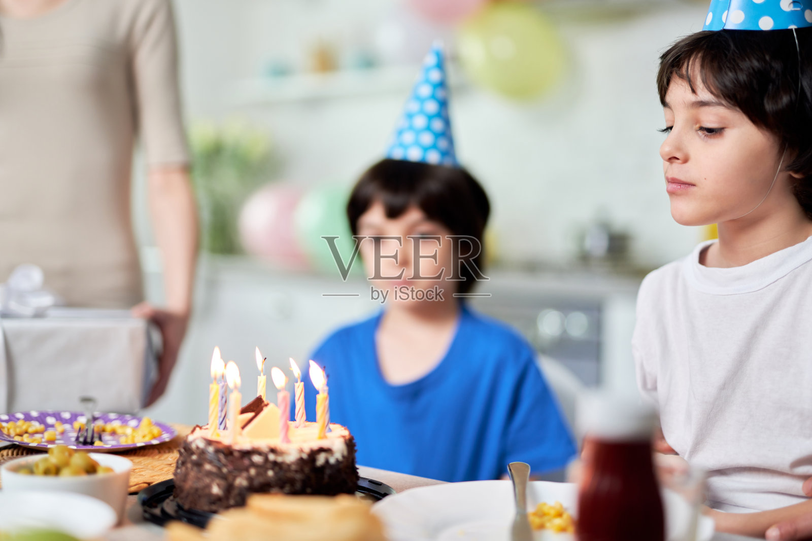 快乐的时刻。小西班牙男孩看着生日蛋糕，许愿，同时准备吹蜡烛的特写。拉丁家庭在家里一起庆祝生日照片摄影图片