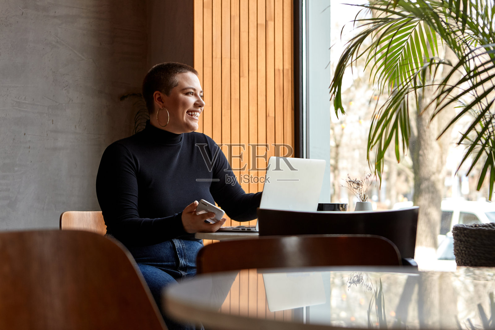 一个留着短发、打了鼻环的年轻女孩正坐在咖啡馆里用笔记本电脑工作。自由职业和远程工作或培训的概念。照片摄影图片