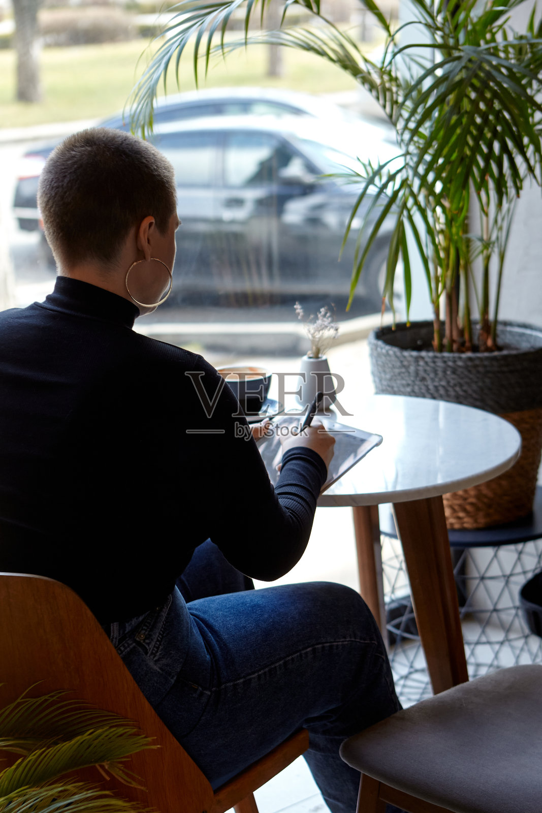 一个留着短发、穿鼻环的年轻女孩坐在咖啡馆里，在平板电脑前工作。自由职业和远程工作的概念。照片摄影图片