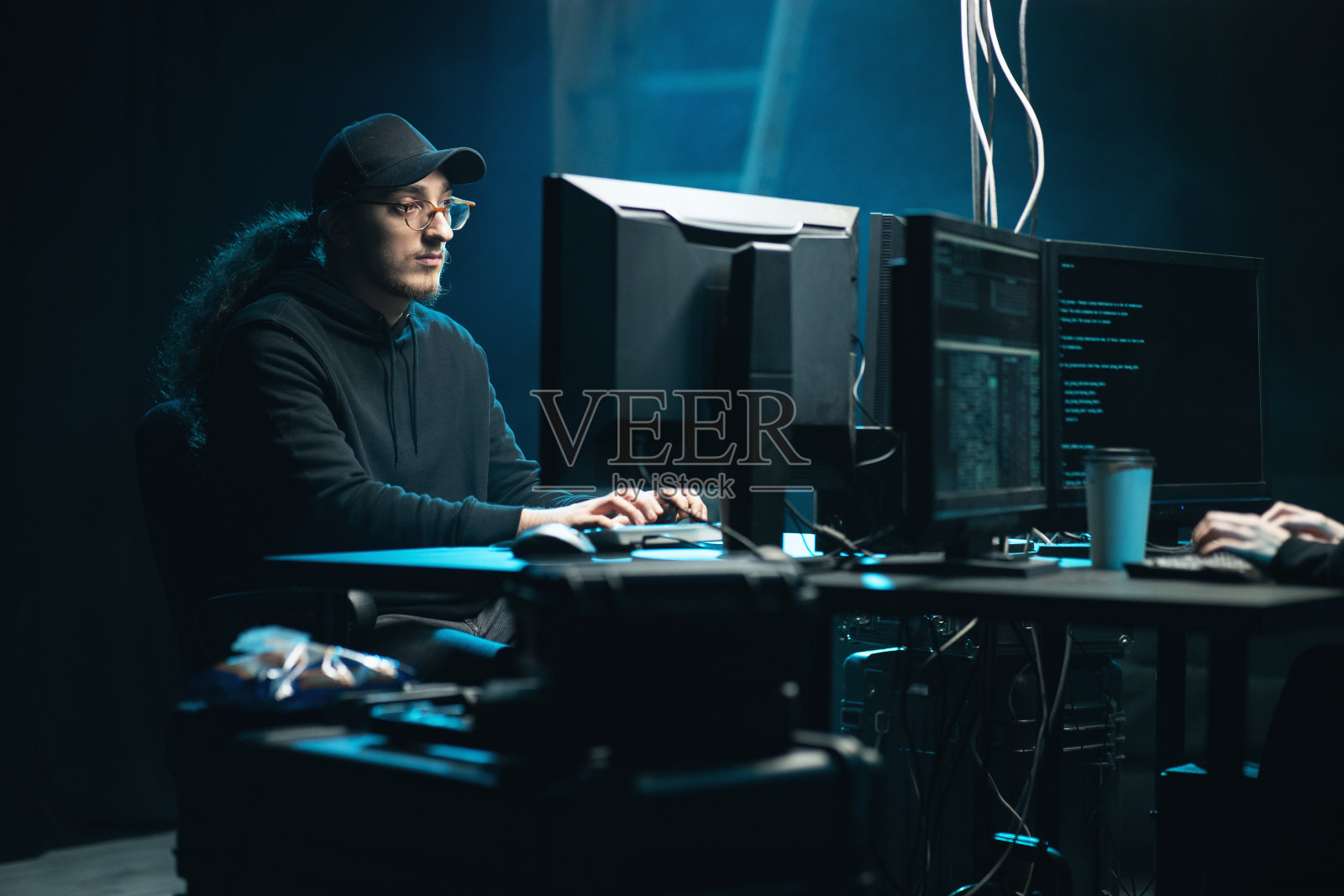 穿着运动衫、戴着棒球帽、戴着眼镜、留着卷发的中年黑客，利用病毒软件和电脑界面进行加密货币欺诈。区块链网络攻击，ddos和恶意软件的概念照片摄影图片