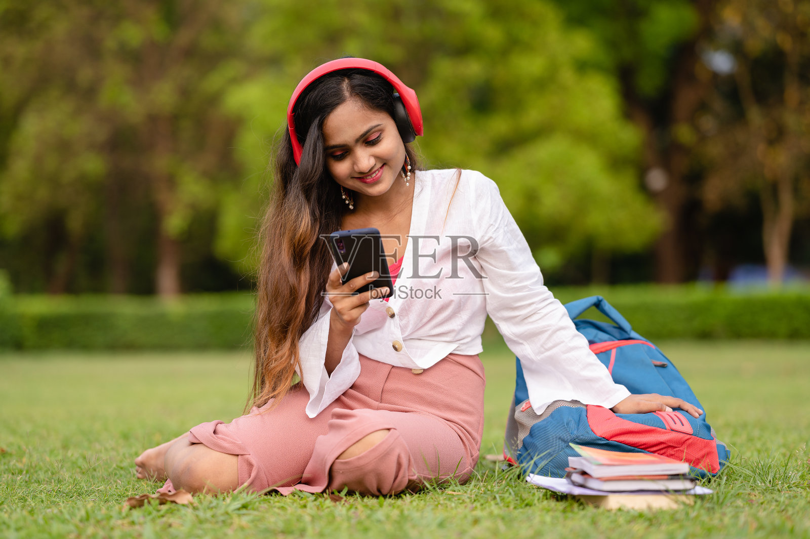 在校园内使用手机和耳机的年轻女学生照片摄影图片