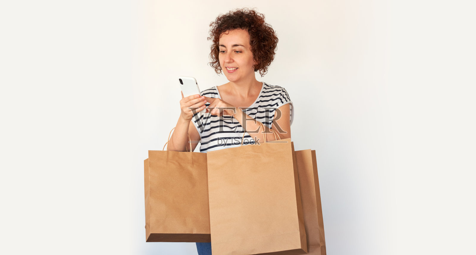 拿着智能手机和购物袋的女人在灰色背景下对着相机摆姿势照片摄影图片