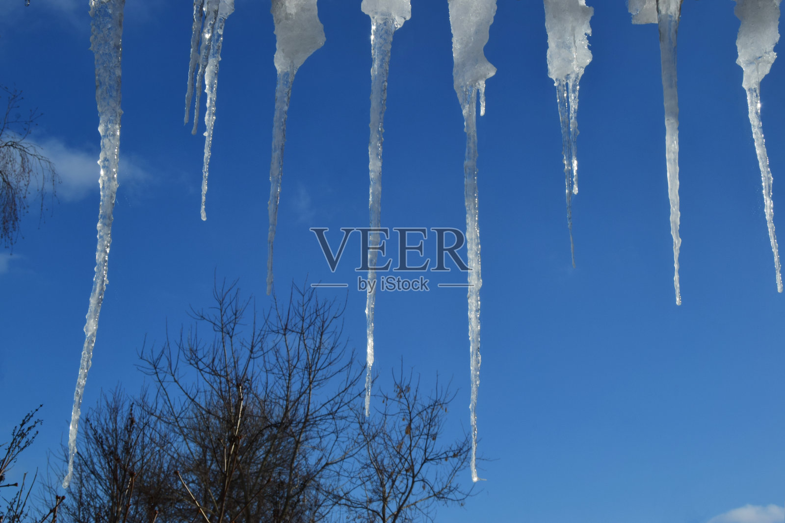 屋顶上挂着冰柱，映衬着湛蓝的天空。春天的景观与冰柱悬挂在屋顶的房子。照片摄影图片