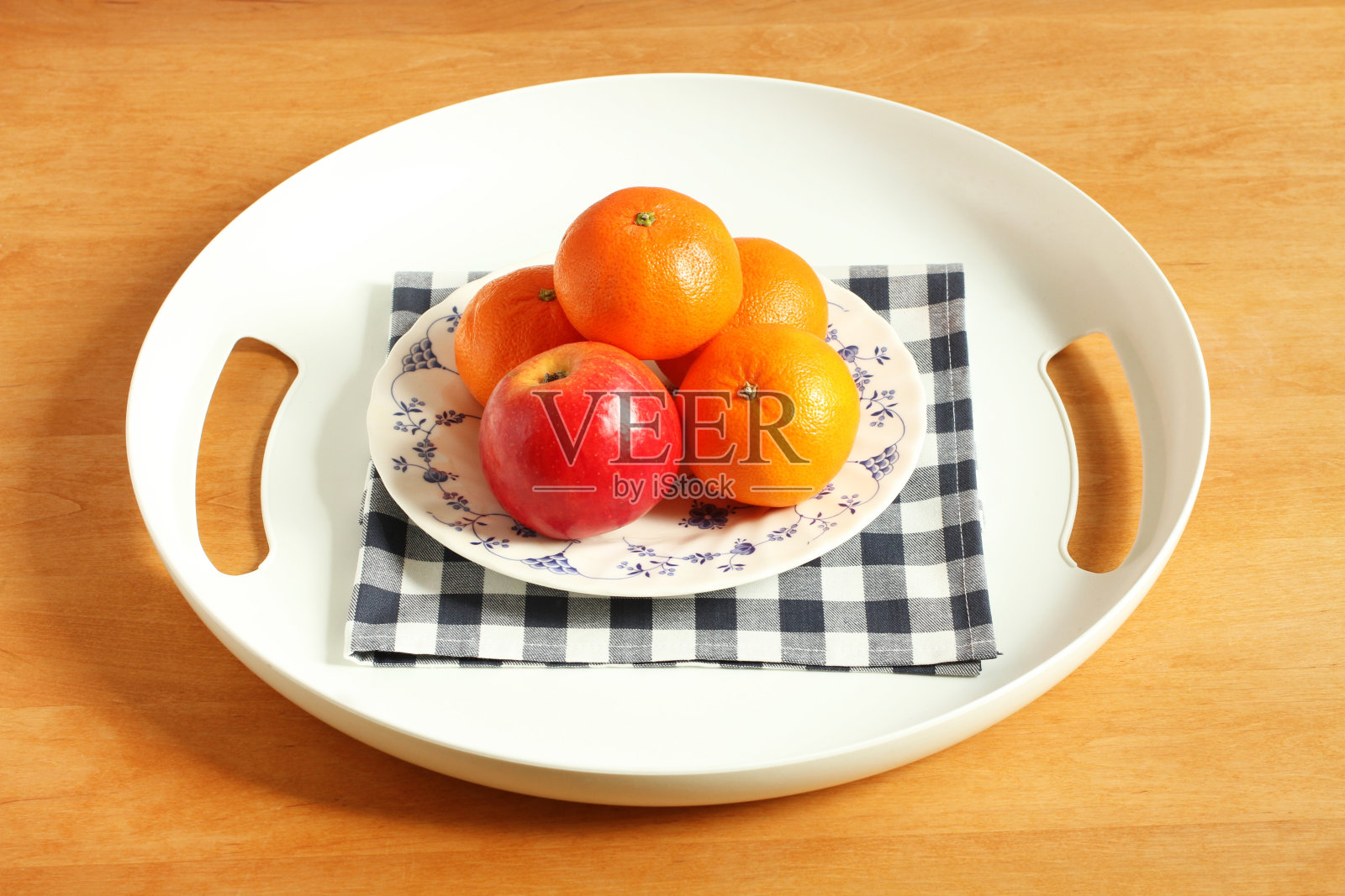 一个白色的塑料托盘，里面装着苹果和橘子，放在一张木桌上。照片摄影图片