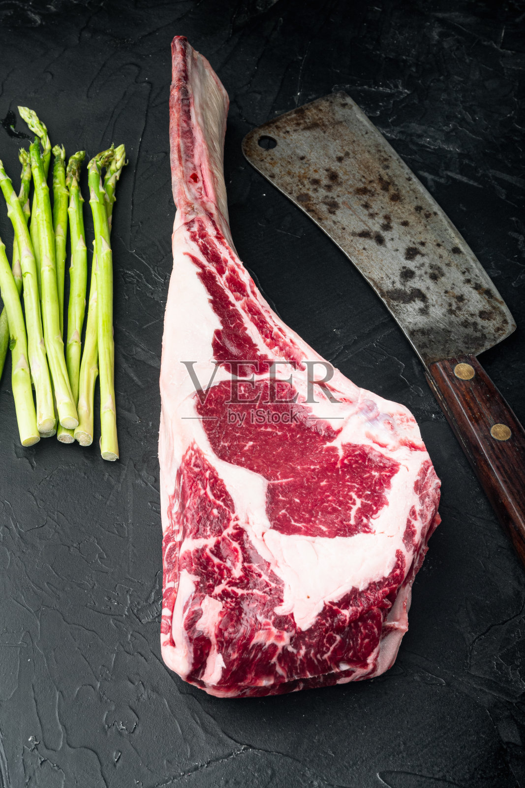 烧烤战斧的大理石牛排，和老屠夫切肉刀，与烧烤材料，在黑色的石头背景照片摄影图片