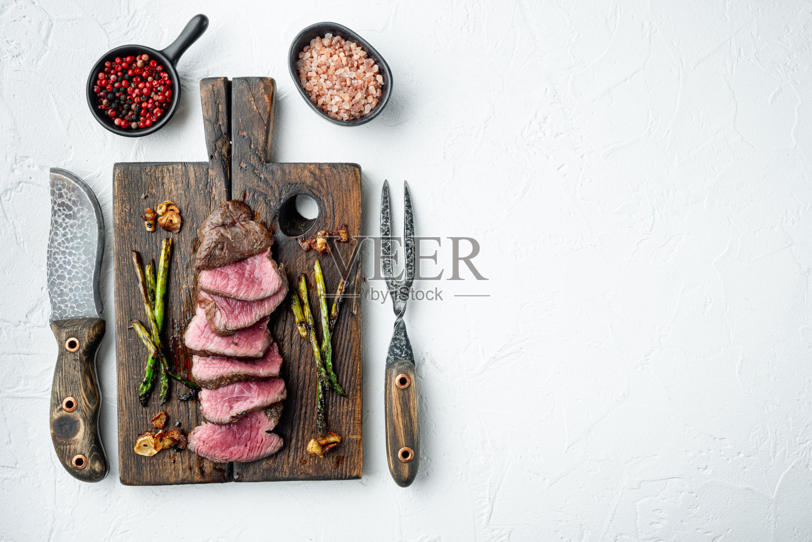 烤菲力牛排，洋葱和芦笋，在木制的服务板上，与肉刀和叉，在白色的石头背景，俯视图平铺，有文字复制空间照片摄影图片