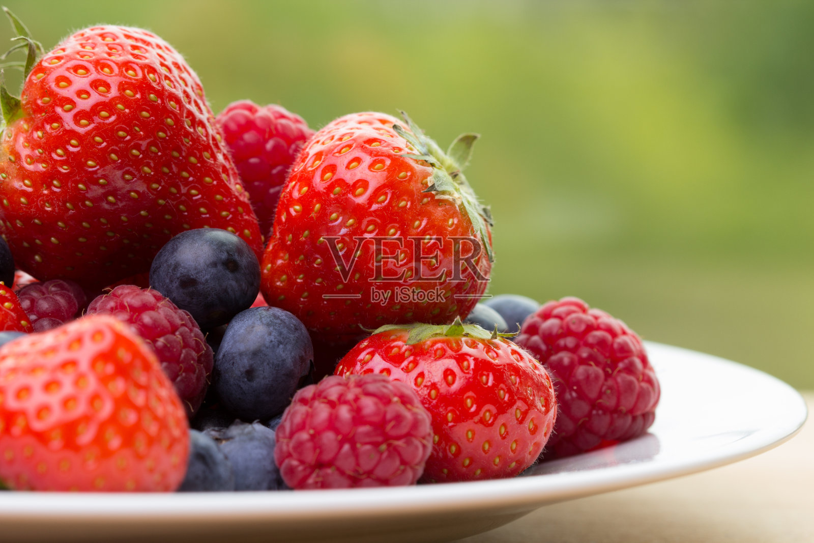 在绿色的背景上堆草莓，蓝莓，覆盆子照片摄影图片