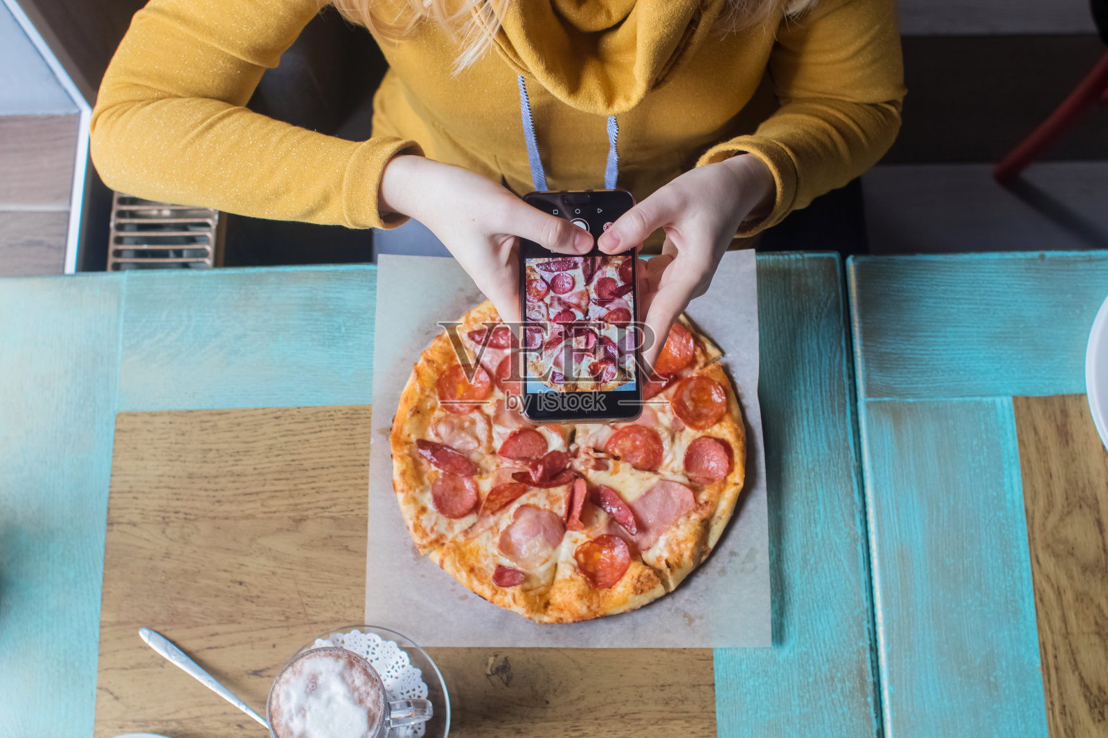 一个博主女孩坐在咖啡馆里用智能手机拍披萨。在社交网络、视频博客和照片博客中工作。创建互联网内容和食物摄影的概念。照片摄影图片