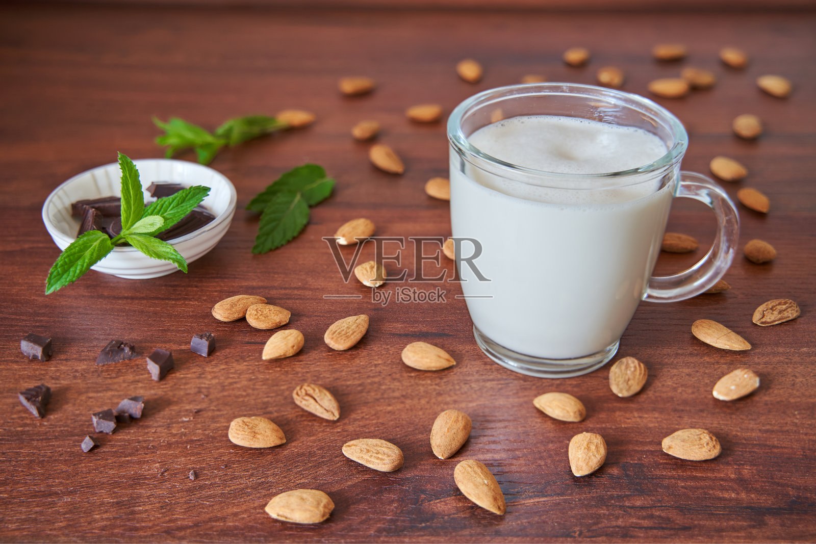 一杯杏仁牛奶。周围是杏仁，黑巧克力和薄荷叶。照片摄影图片