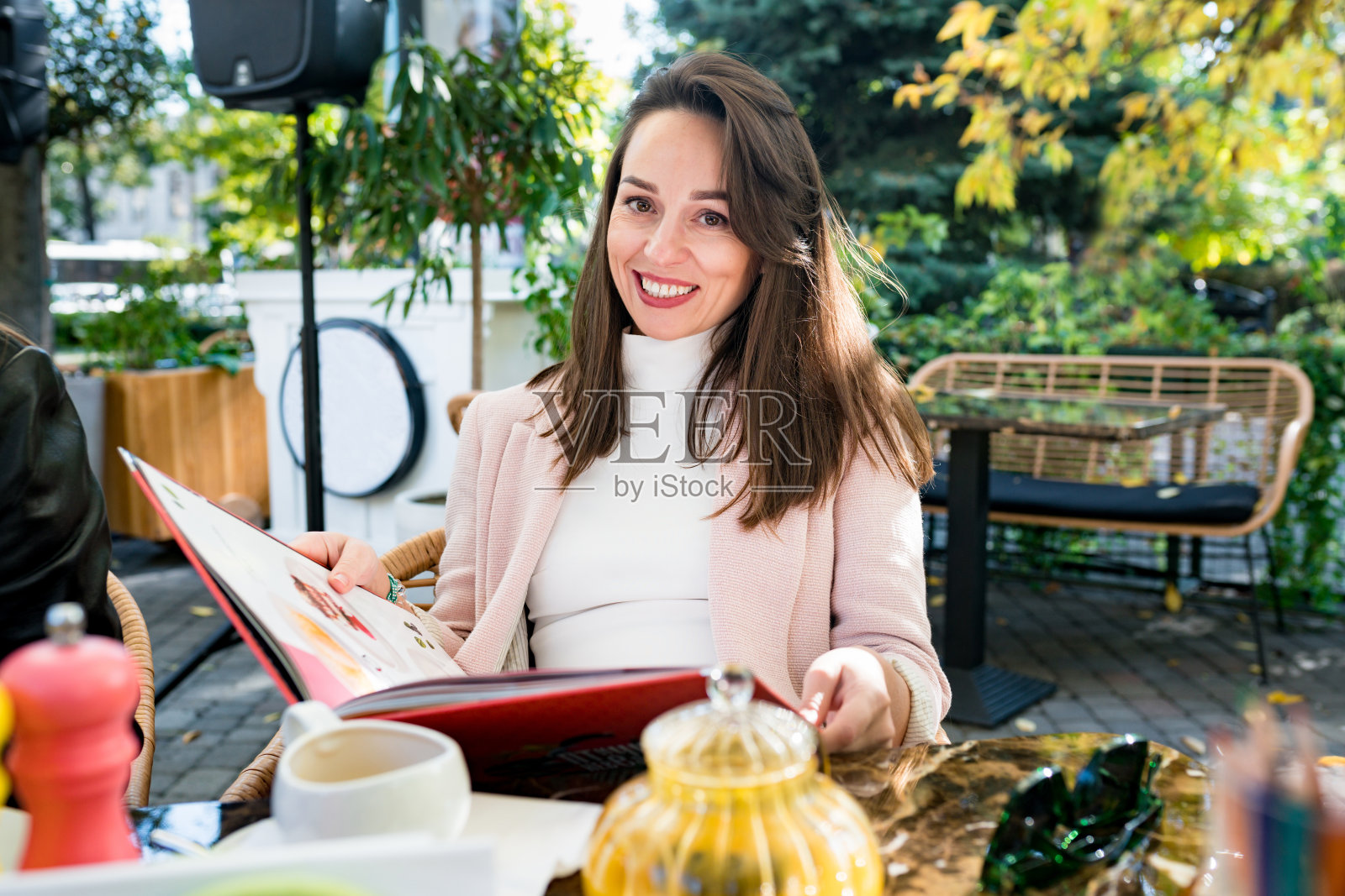 年轻的褐发女人穿着休闲的衣服坐在街上的咖啡馆，一边看着菜单一边选择食物在阳光明媚的日子照片摄影图片