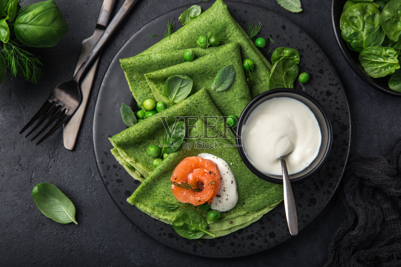 菠菜薄饼与烟熏鲑鱼和酸奶酱在黑色盘子照片摄影图片