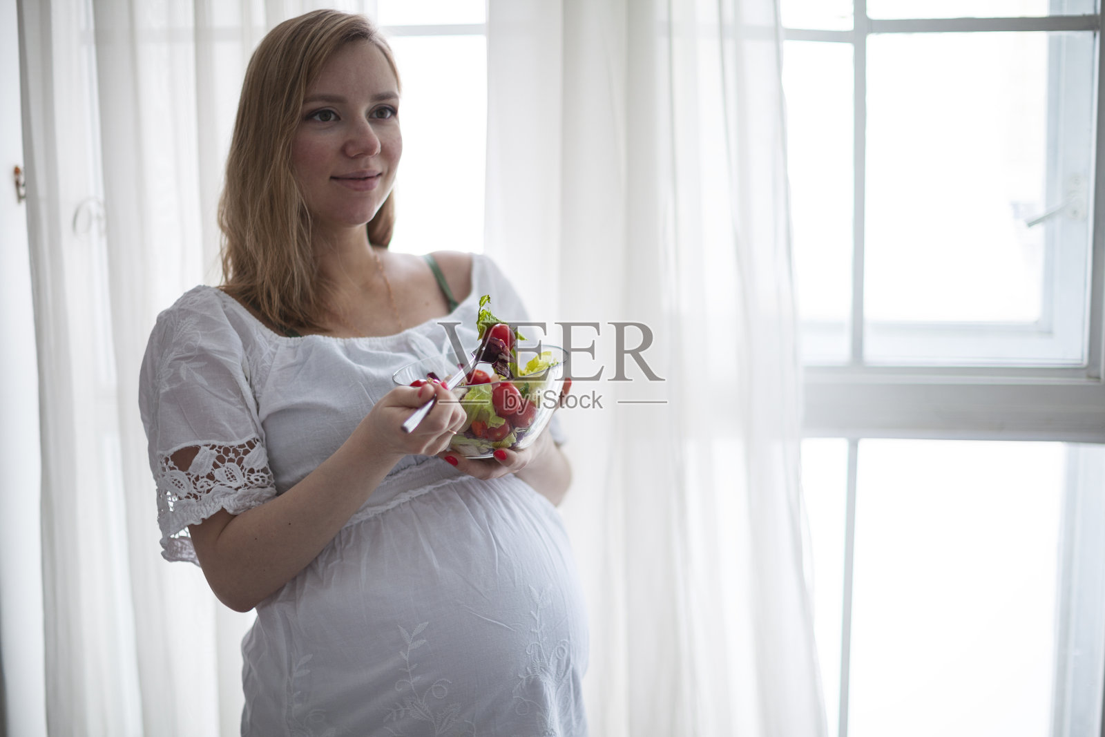 孕妇在家里吃着沙拉微笑着。软焦点照片摄影图片