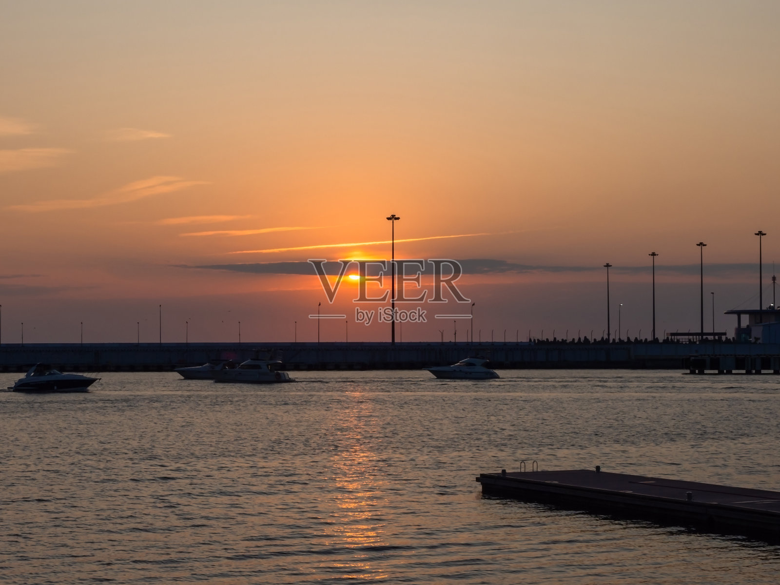天空中的夕阳藏在海面上的云朵后面，游艇在码头上航行照片摄影图片