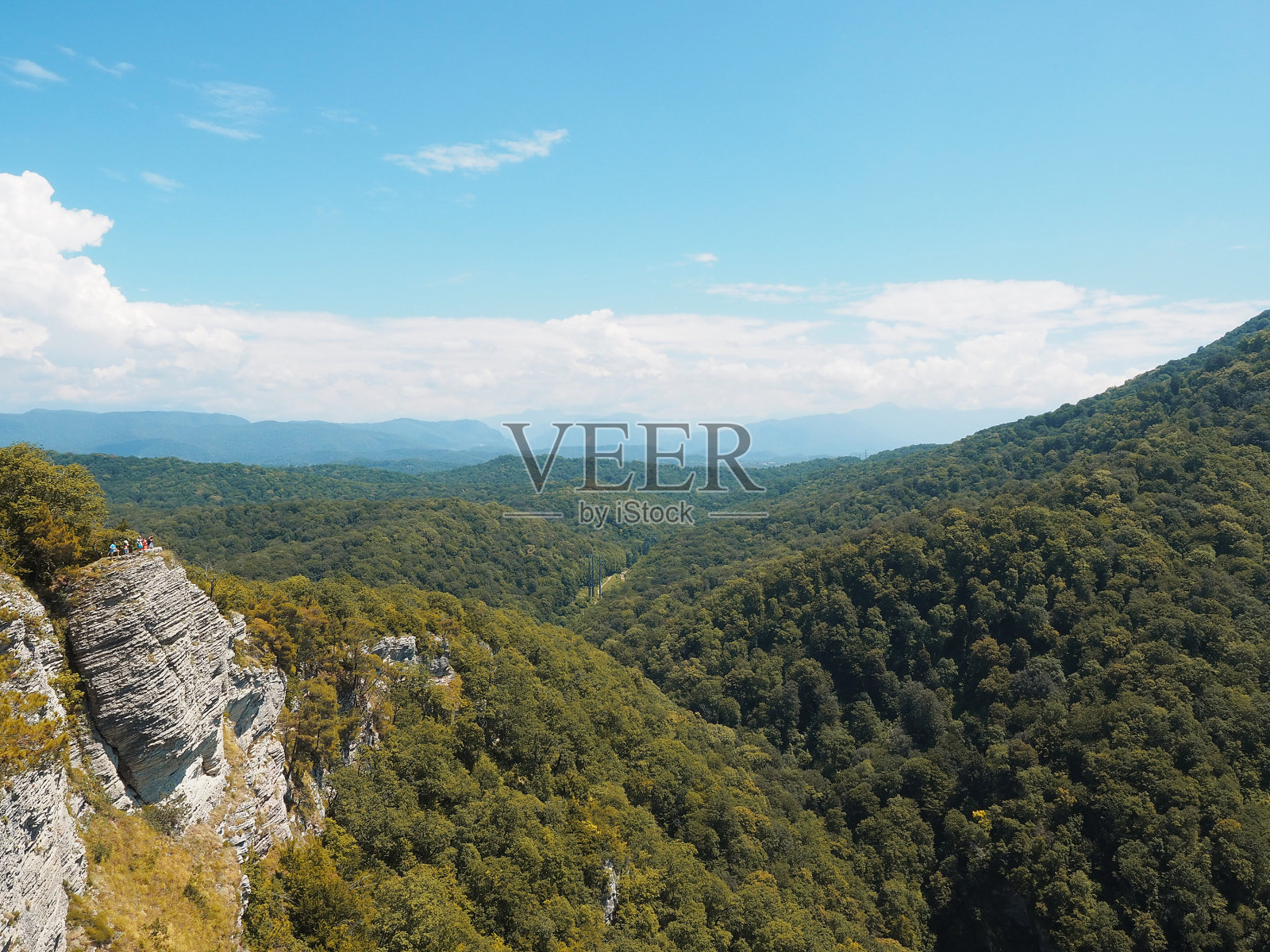 在蓝色的天空和白云的背景下，一个山谷与绿色的森林和岩石悬崖。照片摄影图片