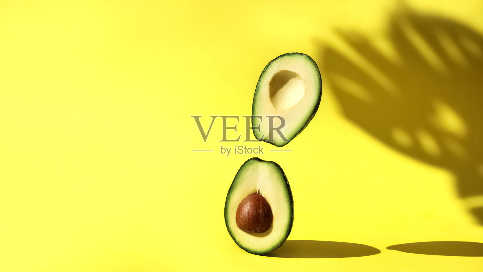 切好的牛油果站在黄色的背景和怪物的叶子和悬浮的影子照片摄影图片