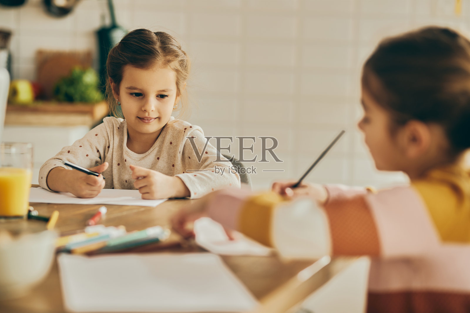 可爱的女孩和她的妹妹在家里的纸上涂色。照片摄影图片