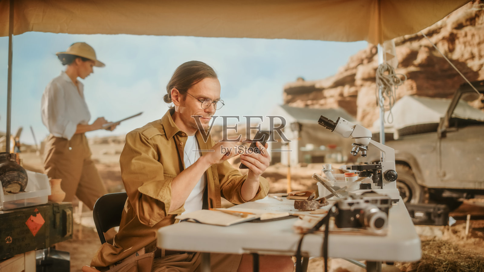 考古挖掘遗址:伟大的男性考古学家做研究，使用智能手机分享发现的化石遗骸，古代文明文化文物在互联网社交媒体上照片摄影图片