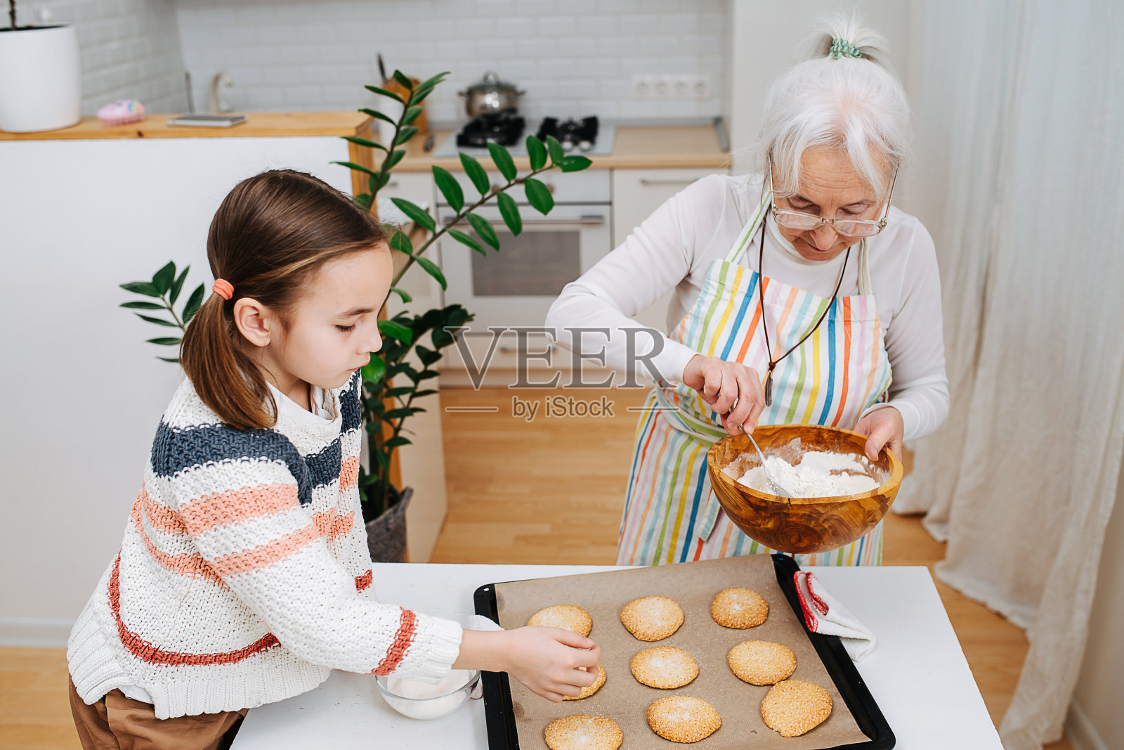 热心的老奶奶在她孙女旁边的新鲜饼干上撒糖粉照片摄影图片