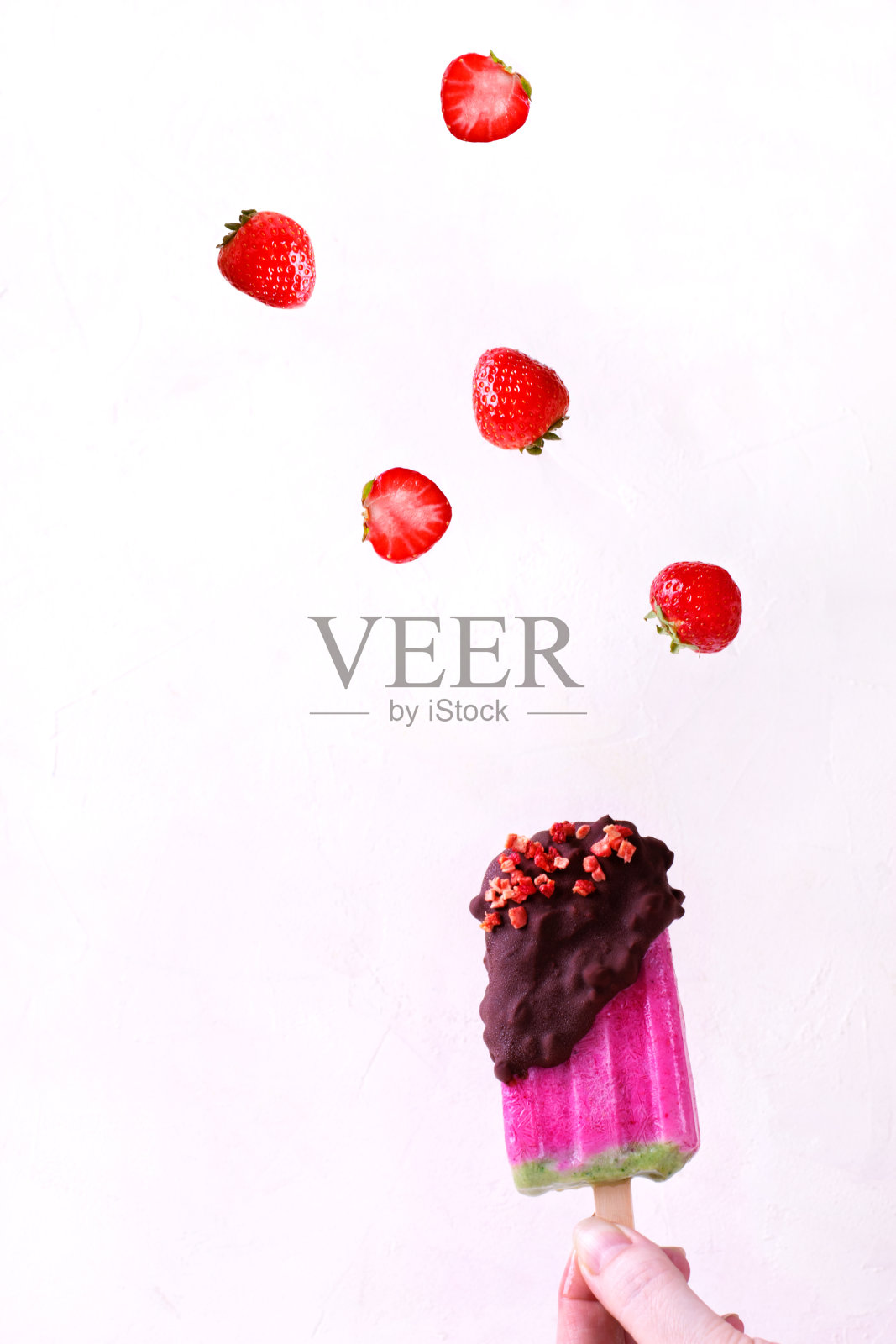 手里拿着巧克力冰棒和飞舞的草莓照片摄影图片