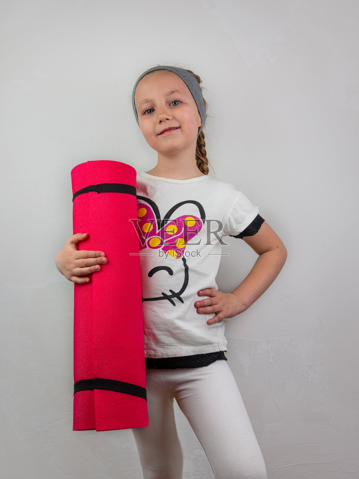 灰色背景下，粉色瑜伽垫的小女孩。瑜伽为儿童心理健康积极的生活方式，运动健身类照片摄影图片