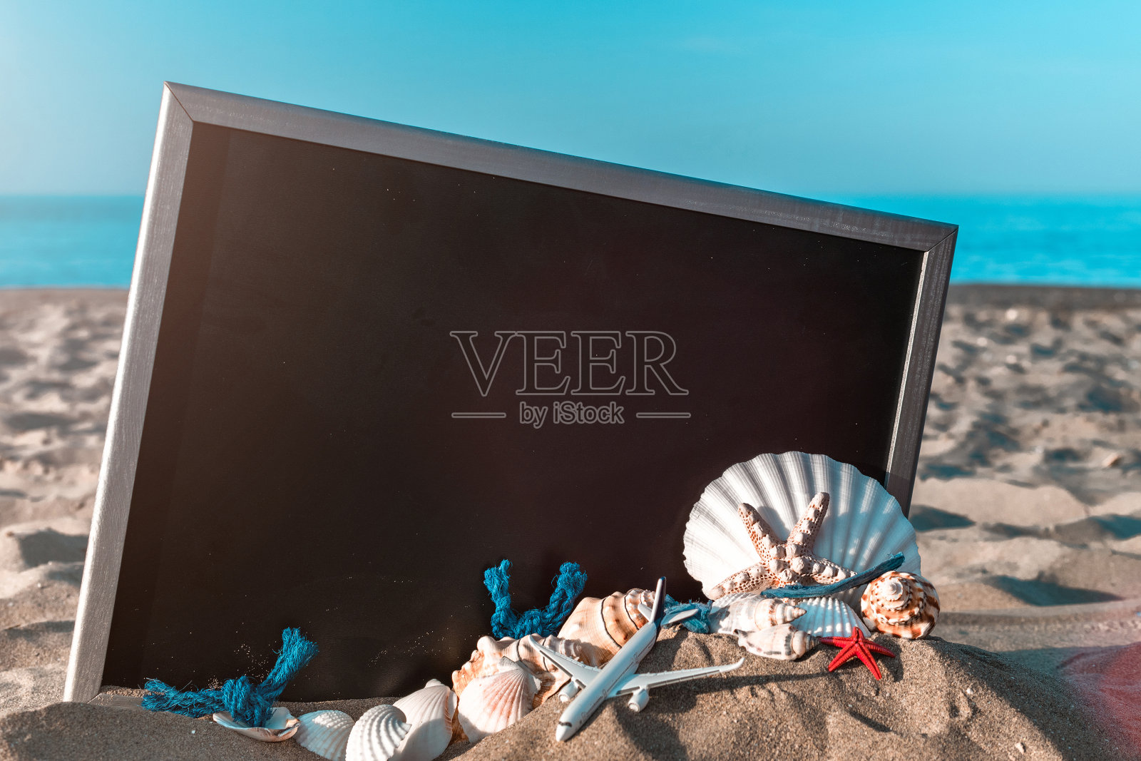 热带的背景。在阳光明媚的日子里，海滩上的黑色书桌旁有地球仪、贝壳、飞机和海星。为文本复制空间。照片摄影图片