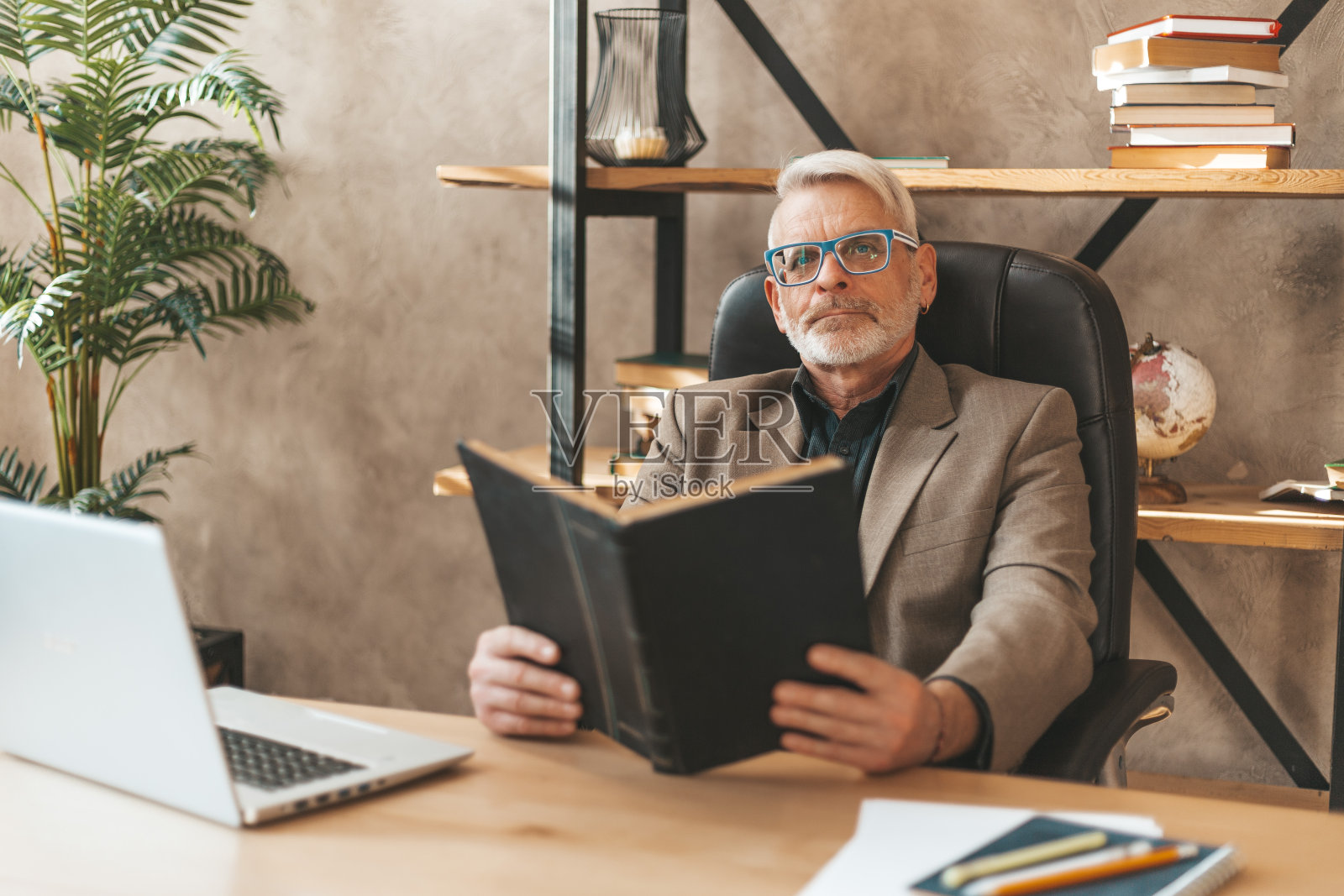 老年学习。梦想着一个拿着书坐在桌前的成熟男人。一个令人不安的问题的答案照片摄影图片