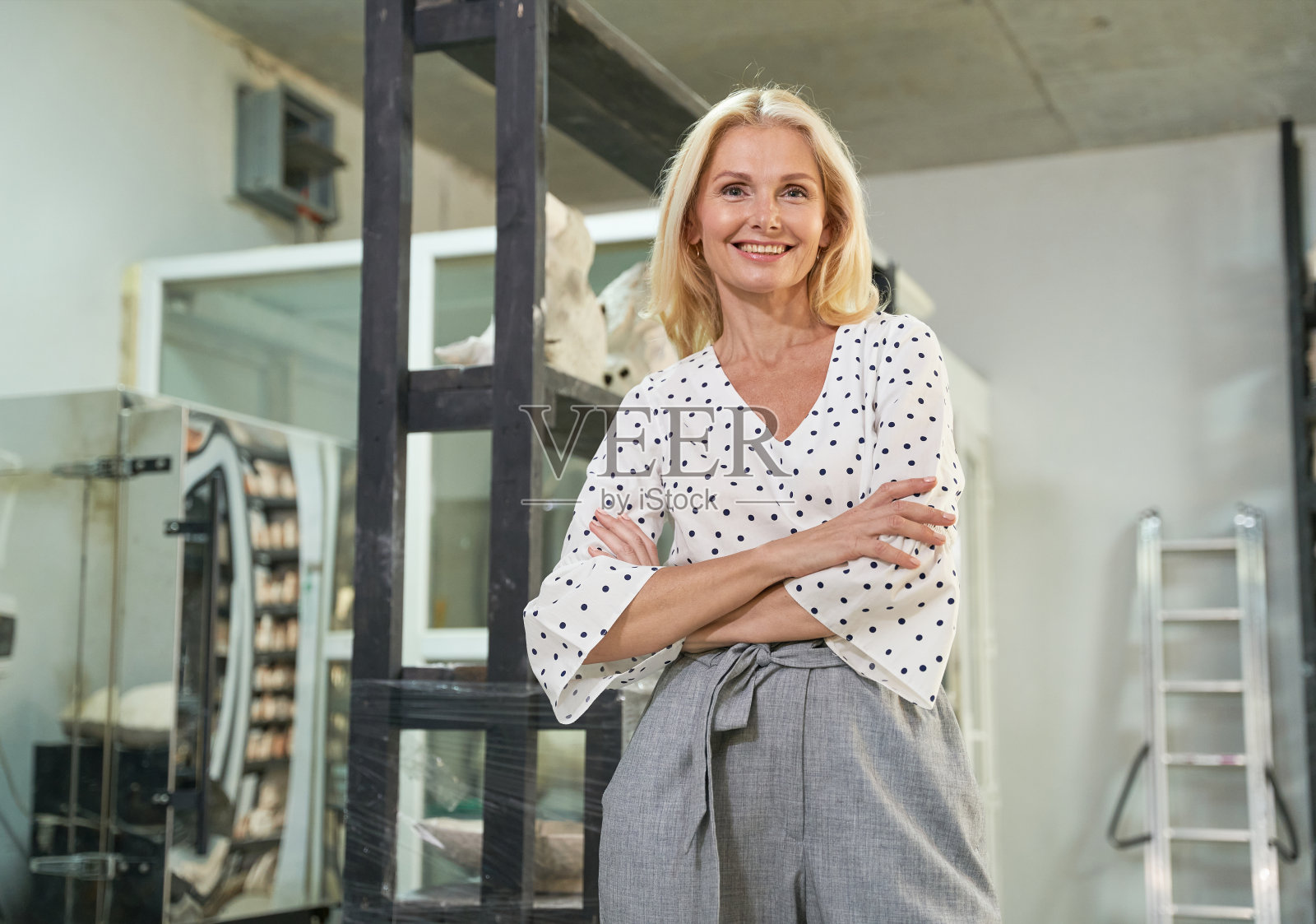 快乐的女企业主对着镜头微笑，双臂交叉站在她的工艺陶器车间摆姿势照片摄影图片