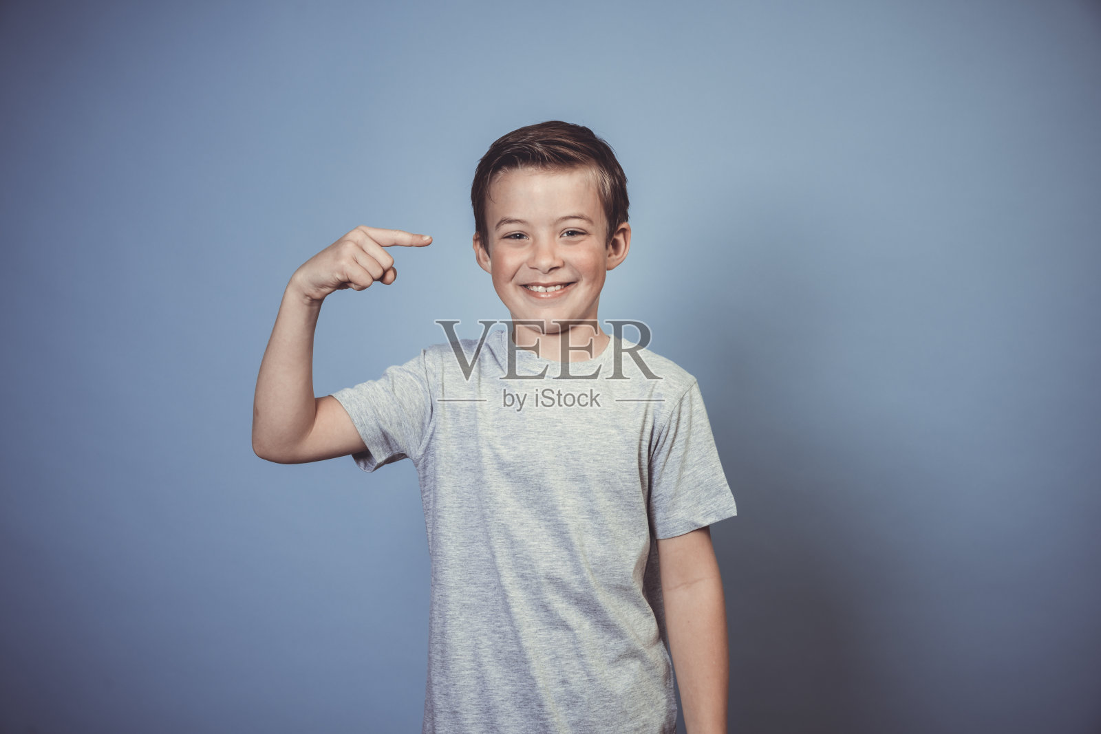 酷，一个穿着灰色t恤的小男孩在蓝色背景前摆姿势照片摄影图片
